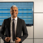 Greg Vales standing in front of stock TV